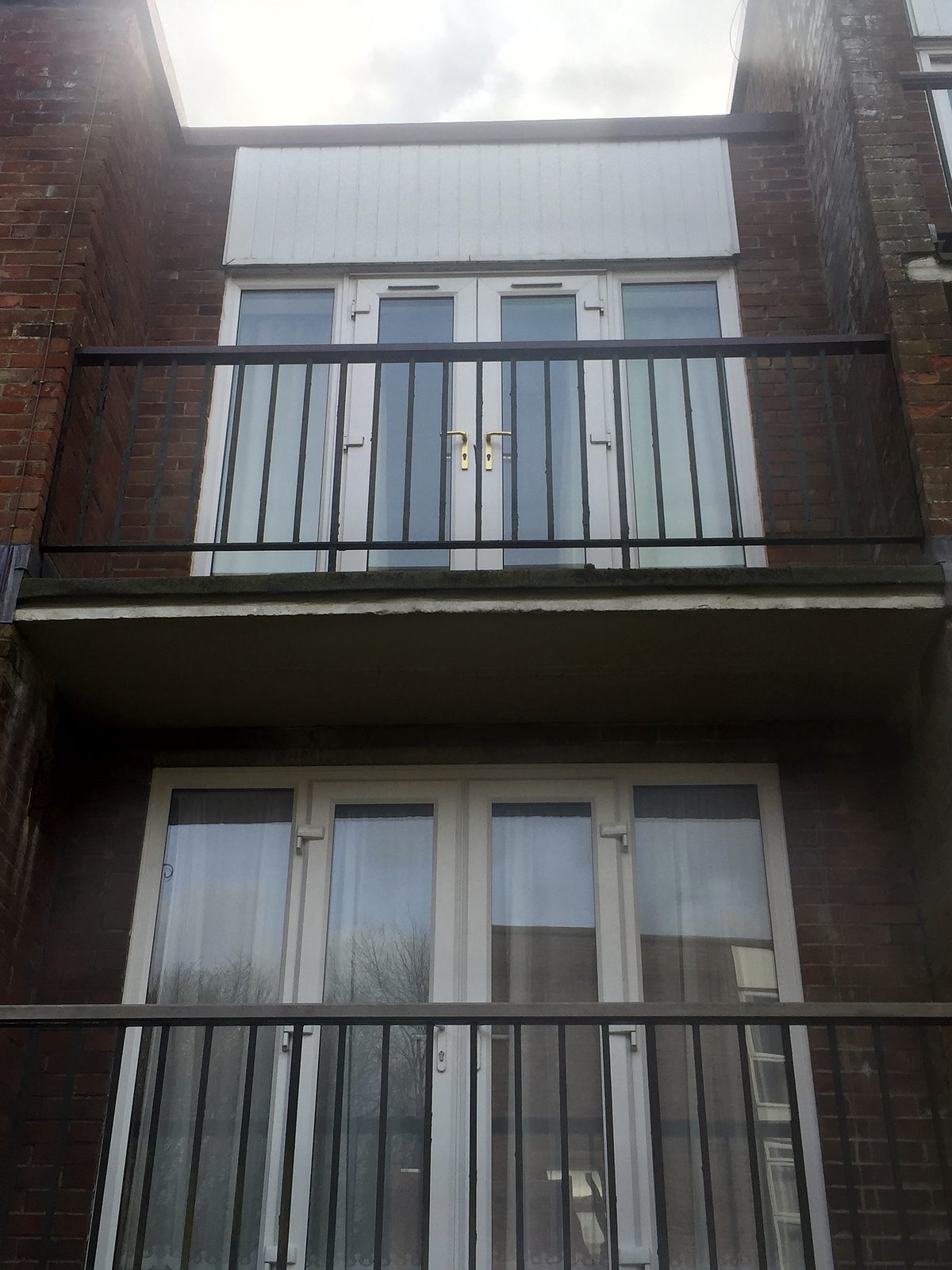 Black steel vertical-bar railings on stacked concrete balconies of a brick block of flats