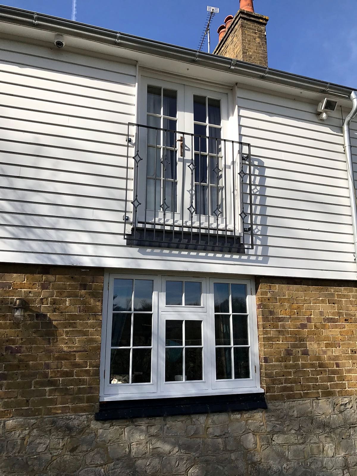 Black steel Juliet balcony at first-floor French doors of a white weatherboarded house