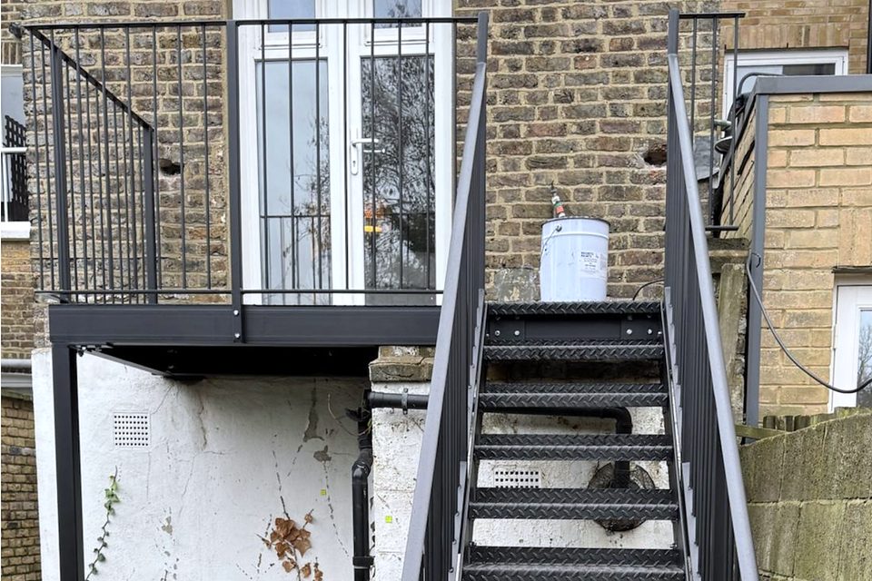 Steel stair with chequer-plate treads climbing from a garden to a first-floor platform outside French doors