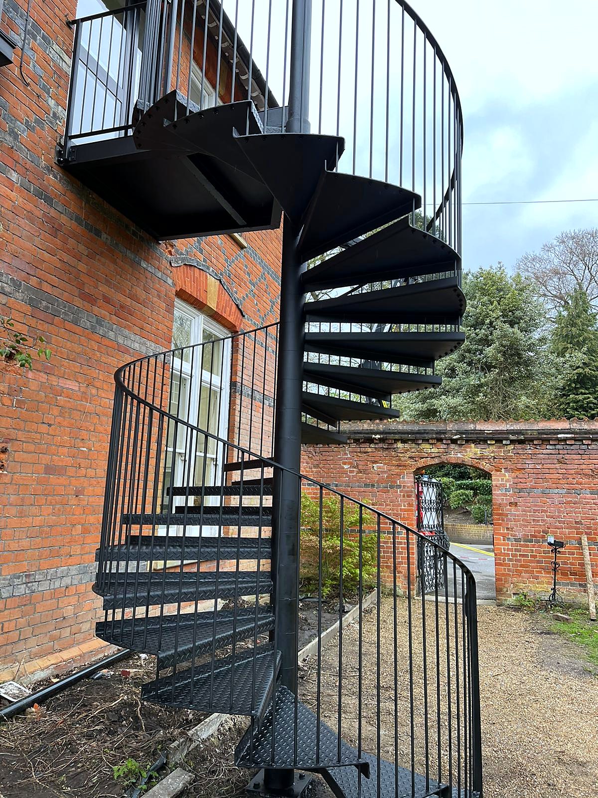 Black steel spiral staircase up to a balcony on a red-brick house