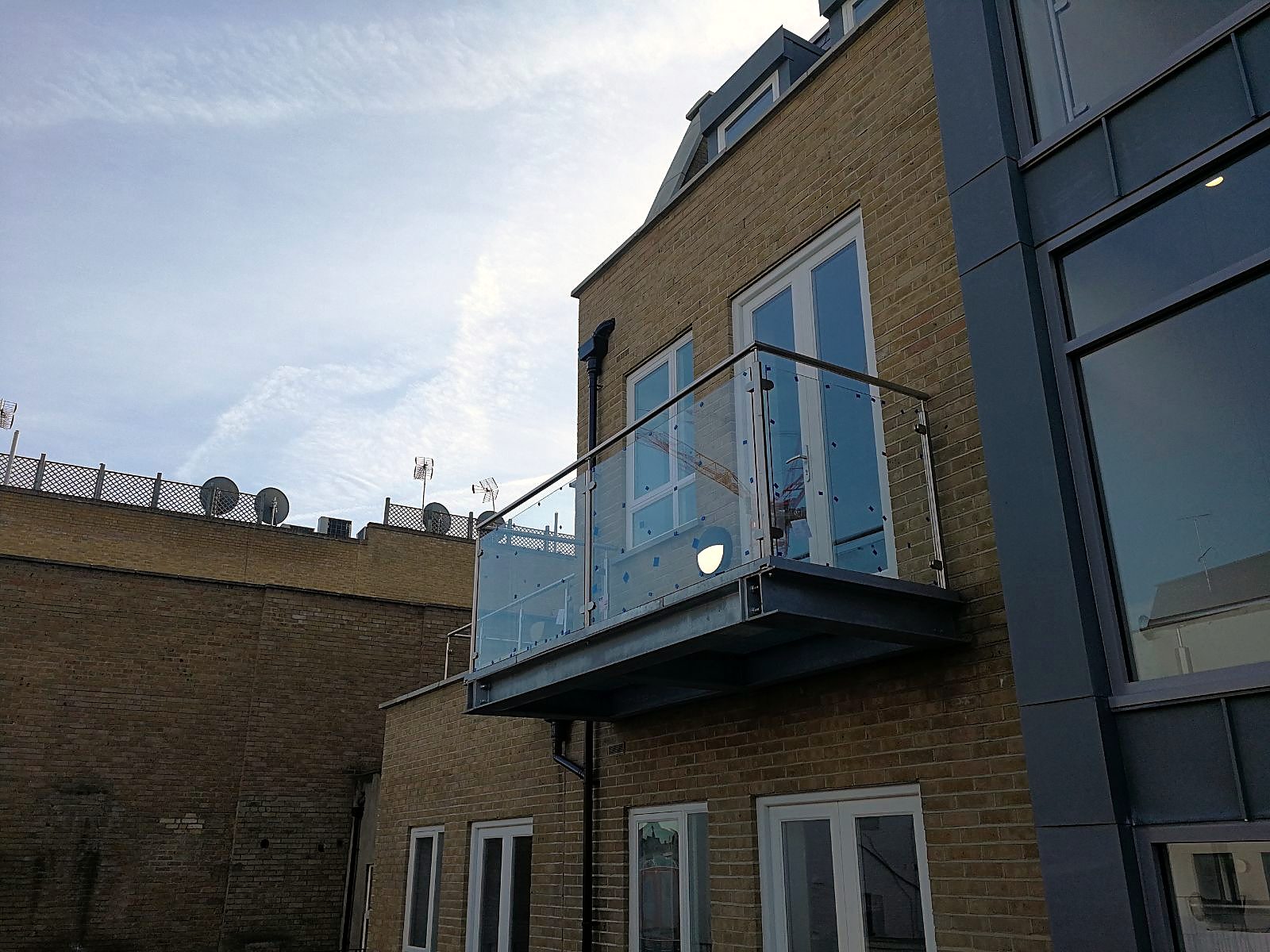 Glass balustrade balcony on a steel base bracketed to a modern brick apartment block