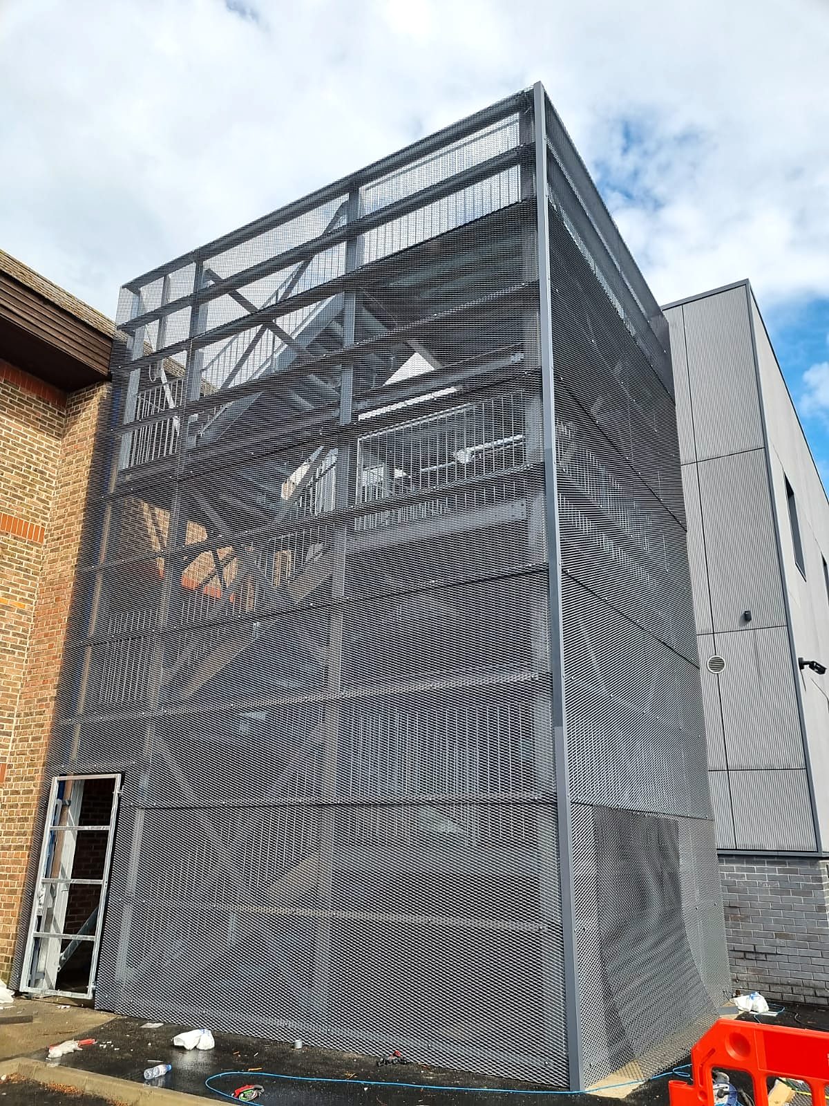 Grey steel escape stair tower clad in perforated mesh panels beside a commercial building