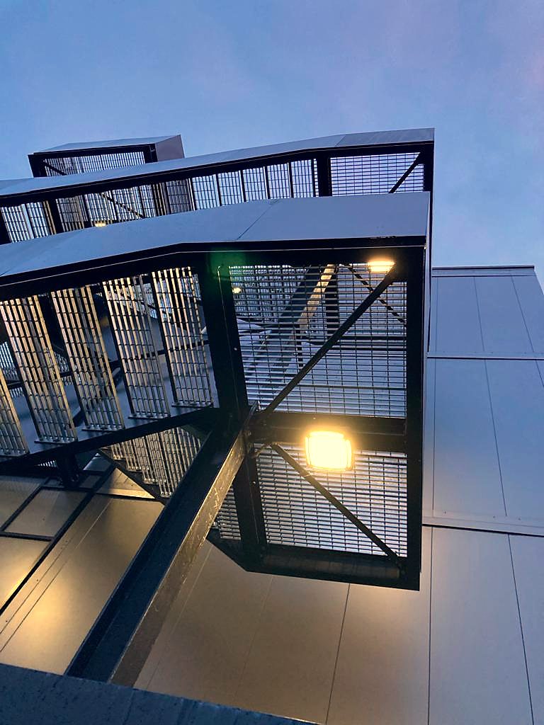 Dark grey steel stair tower with mesh cladding, lit at dusk